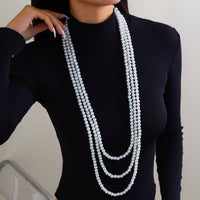 Thumbnail for A woman wearing a black long-sleeve top and a layered pearl necklace with a long chain design.